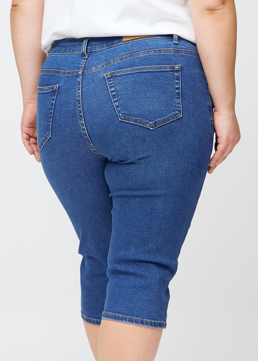 Tæt billede af bagdelen på en plus-size model i mørkeblå denim slim capris – detaljefokus på lommer og syninger.
