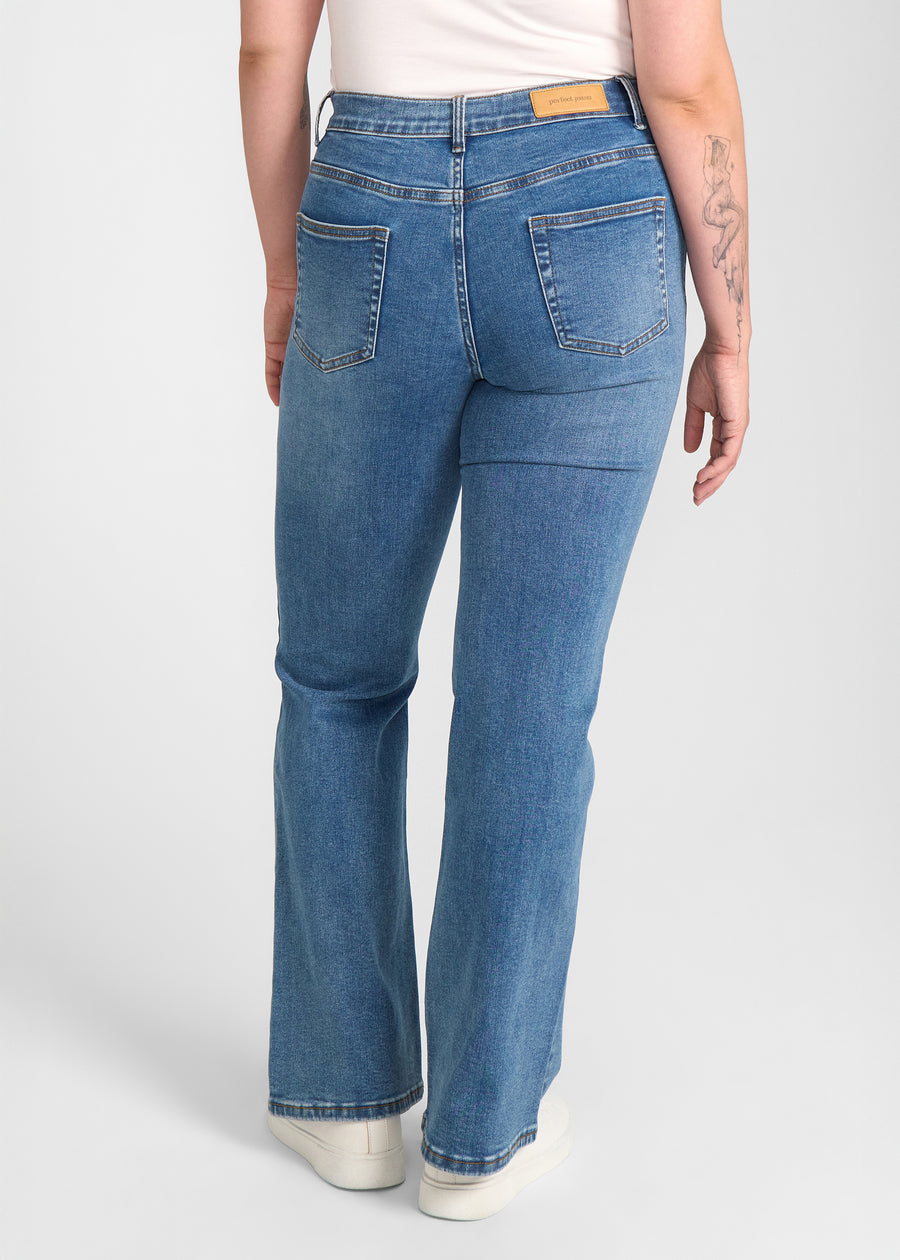 Blå denim bootcut jeans, modelnavn Rivers, som sidder tæt om hofter og lår med et let svaj fra knæet og ned, set bagfra, så man kan se hele produktet. på en plus-size model.