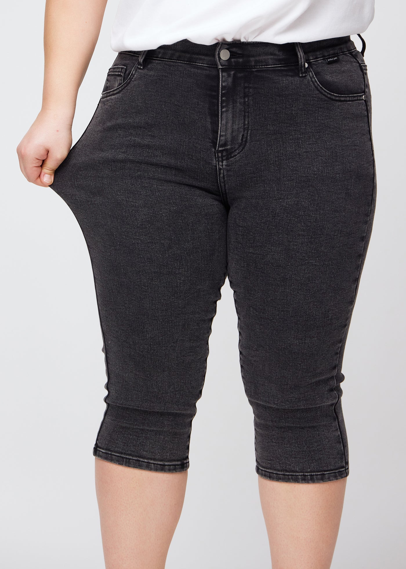 Plus-size model strækker caprisene ved låret for at vise stretch.