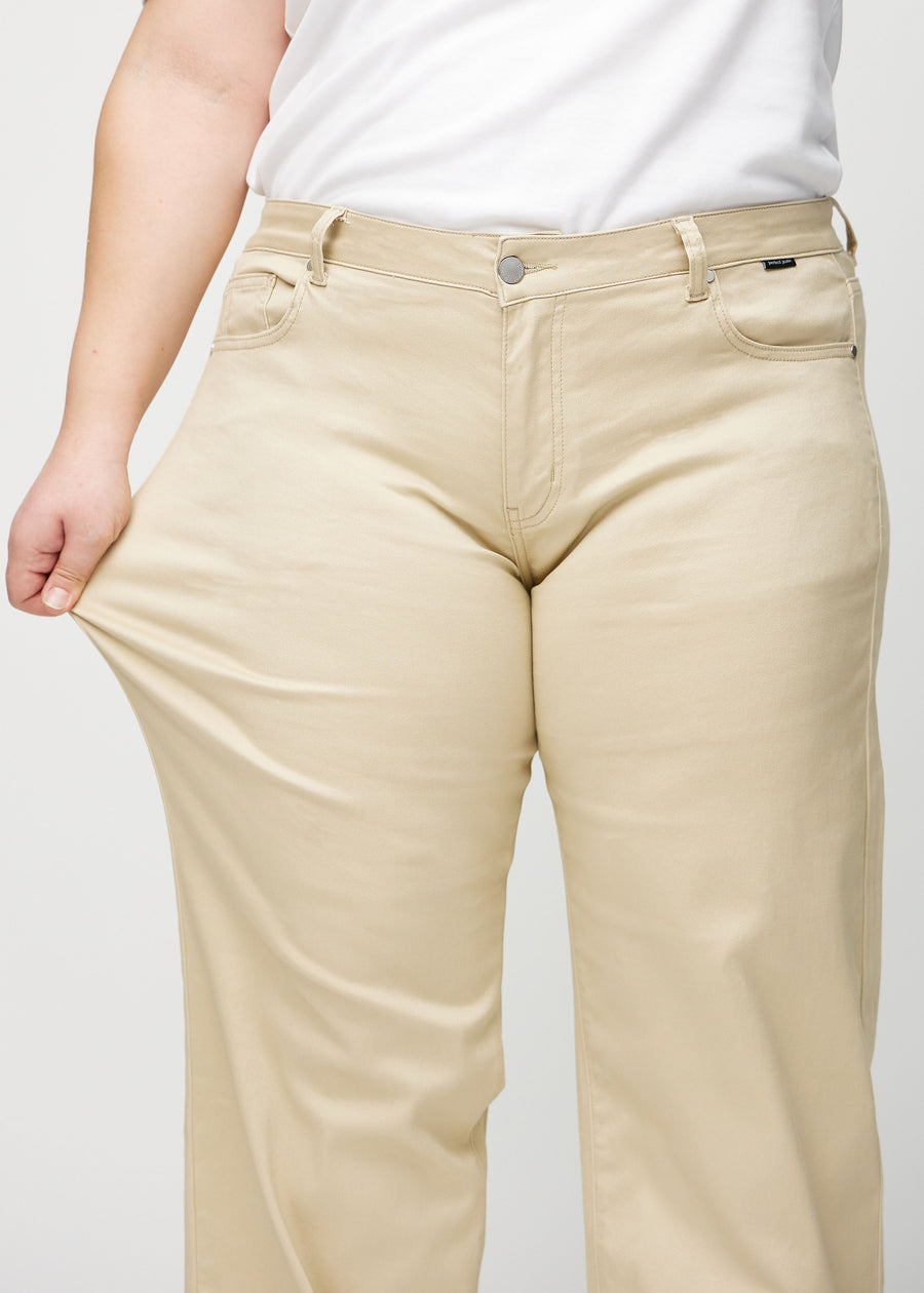 Plus-size model strækker jeansene ved låret for at vise stretch.