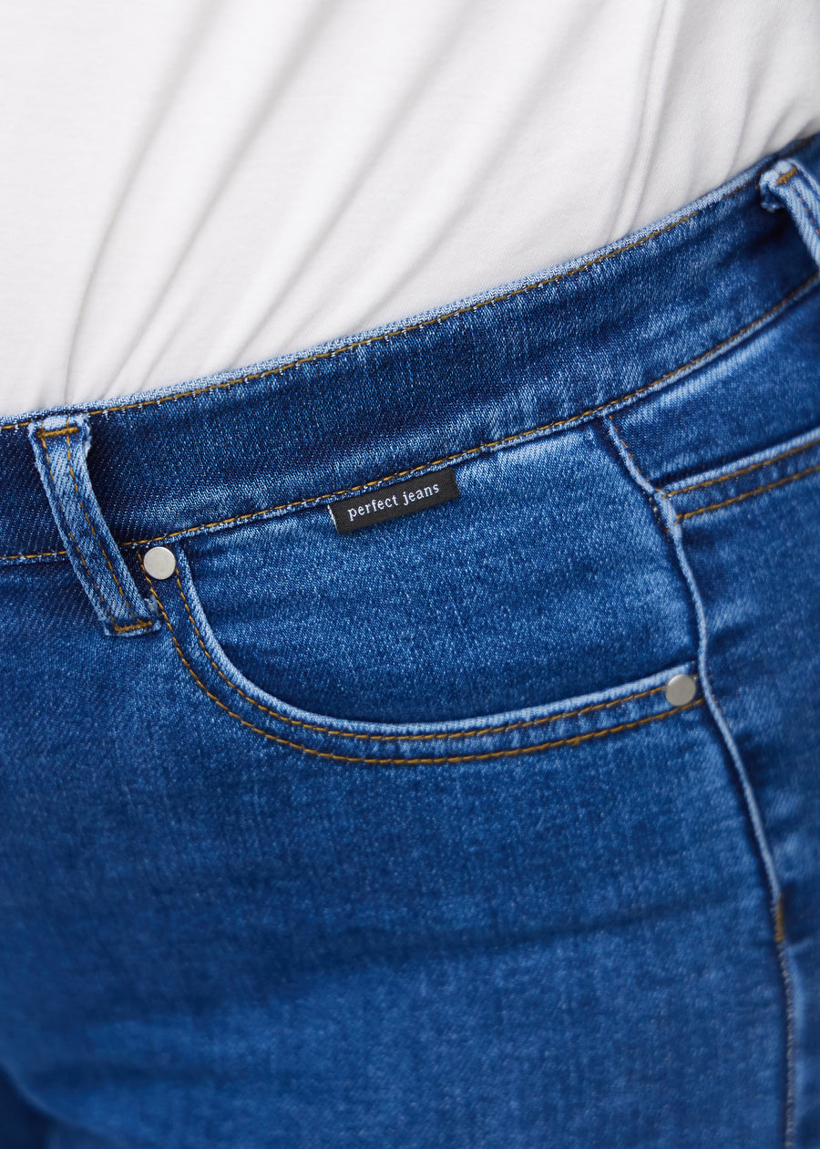 Nahaufnahme von dunkelblauem Denim mit Perfect Jeans Logoetikett an der Vorderkante der Tasche auf einem Plus-Size-Modell.