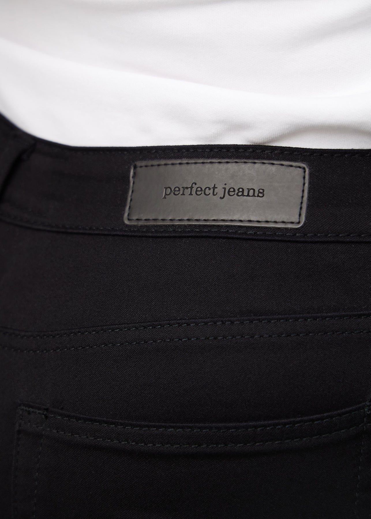 Nærbillede af sort jeansmateriale med Perfect Jeans læderpatch bagpå i taljen, på en plus-size model.