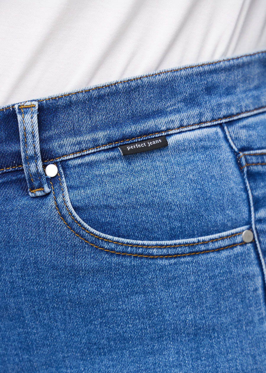 Nahaufnahme von blauem Denim mit Perfect Jeans Logoetikett an der Vorderkante der Tasche auf einem Plus-Size-Modell.