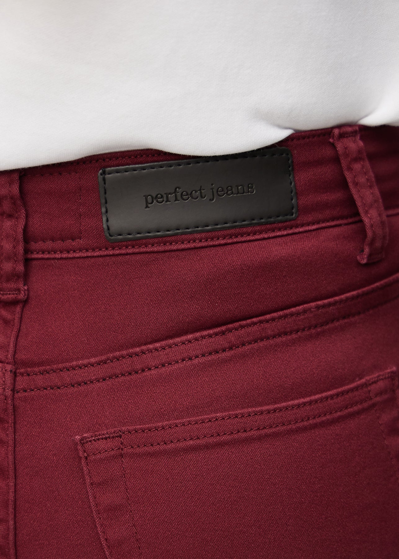 Nærbillede af rødt jeansmateriale med Perfect Jeans læderpatch bagpå i taljen.