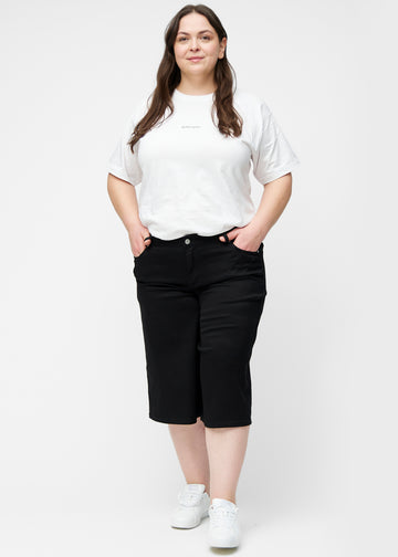 Fuldt billede af plus-size model i løse, sorte capris i farven Ravens, der går til lige under knæet.