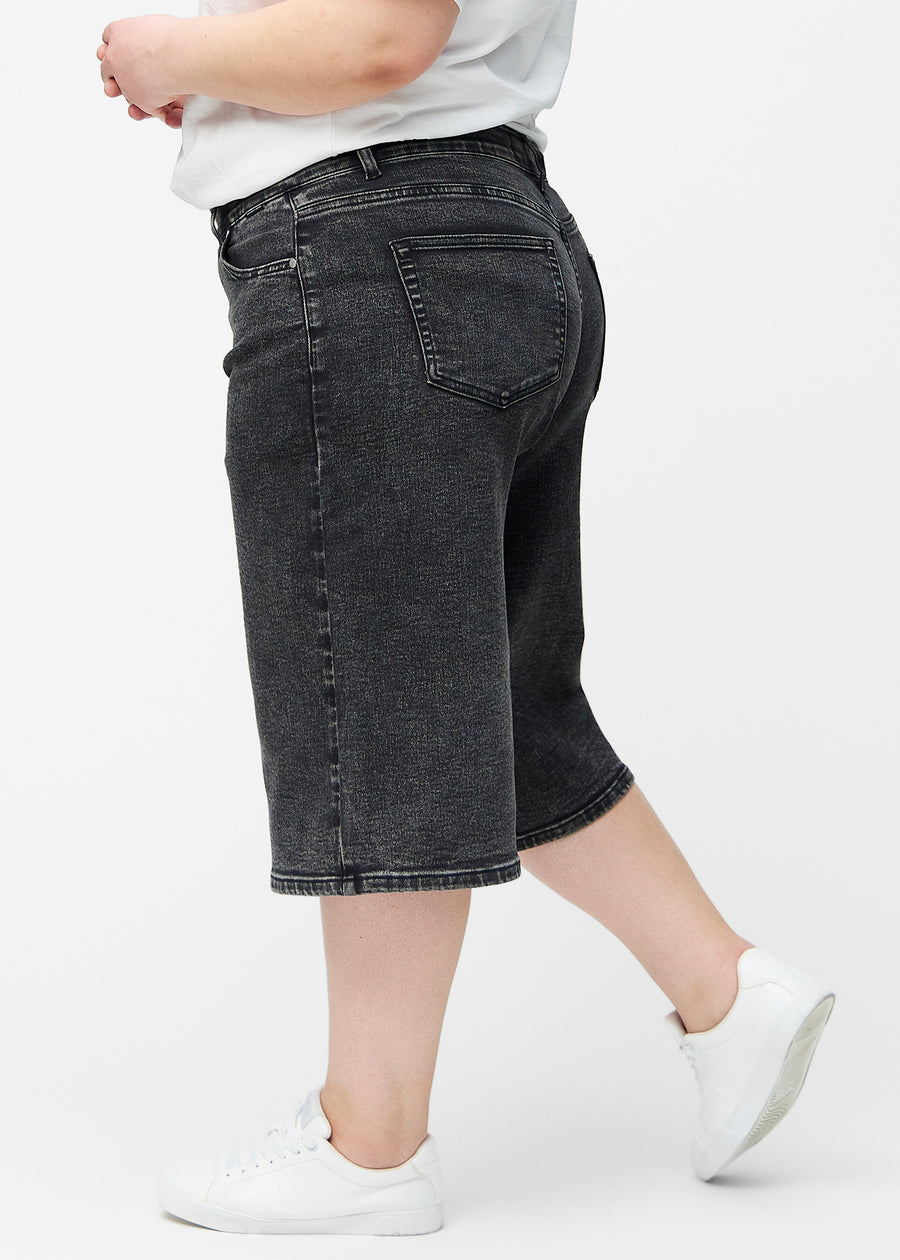 Løse, mørkegrå denim capris i farven Shadows set fra siden på plus-size model, hvor den brede pasform og længden til lige under knæet er synlig.