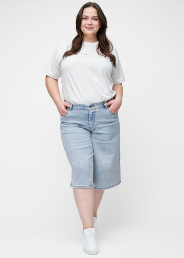 Ganzkörperbild des Plus-Size-Models in lockeren, hellblauen Denim-Capris in der Farbe Waves, die bis knapp unter das Knie reichen.