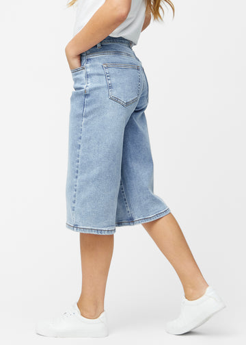 Lockere, hellblaue Denim-Capris in der Farbe Waves von der Seite am Model, wobei die weite Passform und die Länge bis knapp unter das Knie sichtbar sind.