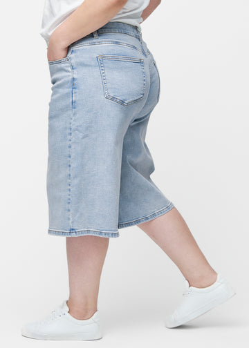 Lockere, hellblaue Denim-Capris in der Farbe Waves von der Seite am Plus-Size-Model, wobei die weite Passform und die Länge bis knapp unter das Knie sichtbar sind.