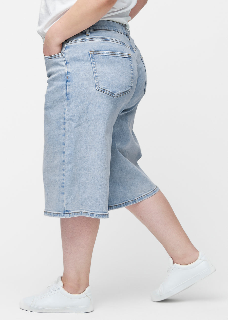 Lockere, hellblaue Denim-Capris in der Farbe Waves von der Seite am Plus-Size-Model, wobei die weite Passform und die Länge bis knapp unter das Knie sichtbar sind.