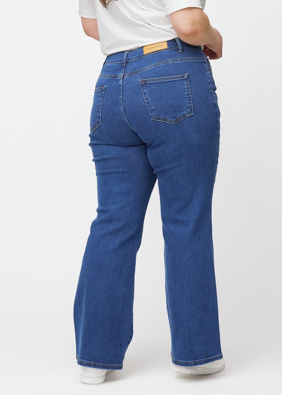 Dunkelblaue Mid-Rise-Bootcut-Jeans in der Farbe Oceans. Rückansicht an einem Plus-Size-Model, die gesamte Passform ist zu sehen.
