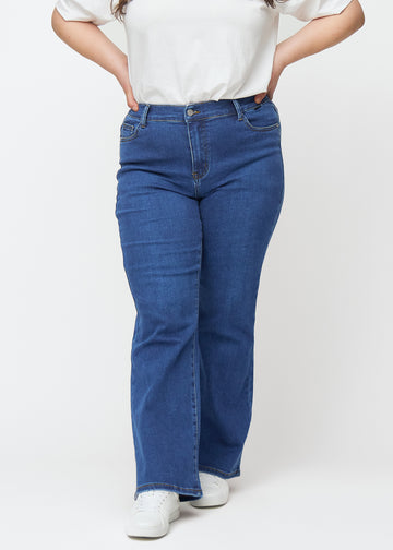 Dunkelblaue Mid-Rise-Bootcut-Jeans in der Farbe Oceans. Vorderansicht an einem Plus-Size-Model, an Hüfte und Oberschenkeln anliegend mit leicht ausgestelltem Bein.