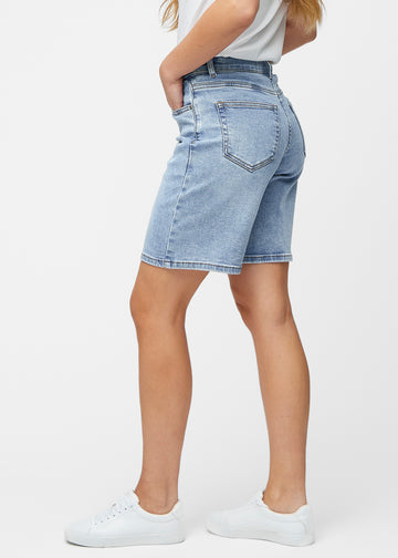 Lockere, hellblaue Denim-Shorts in der Farbe Waves von der Seite am Model, wobei die weite Passform und die Länge bis knapp über das Knie sichtbar sind.
