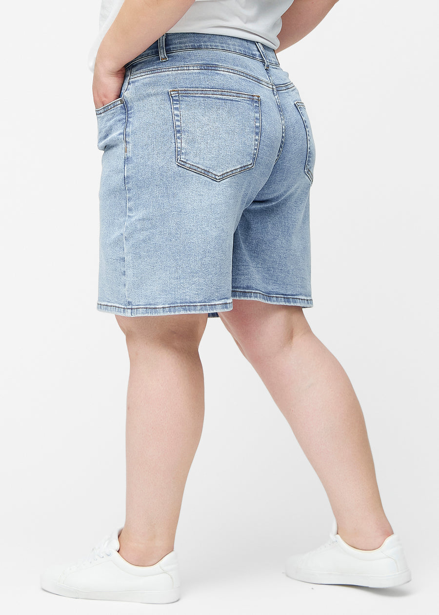 Lockere, hellblaue Denim-Shorts in der Farbe Waves von der Seite am Plus-Size-Model, wobei die weite Passform und die Länge bis knapp über das Knie sichtbar sind.
