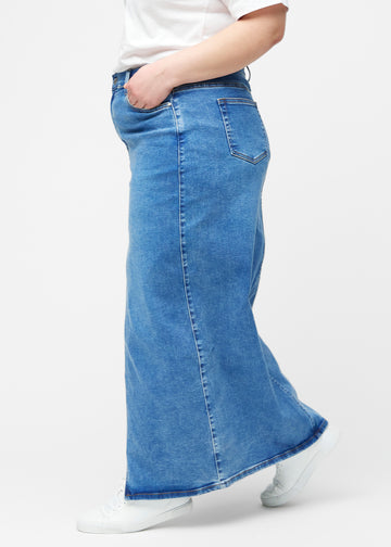 Lang, klassisk blå denimnederdel i farven Rivers med regulær pasform set fra siden på plus-size model, med synligt slids foran.
