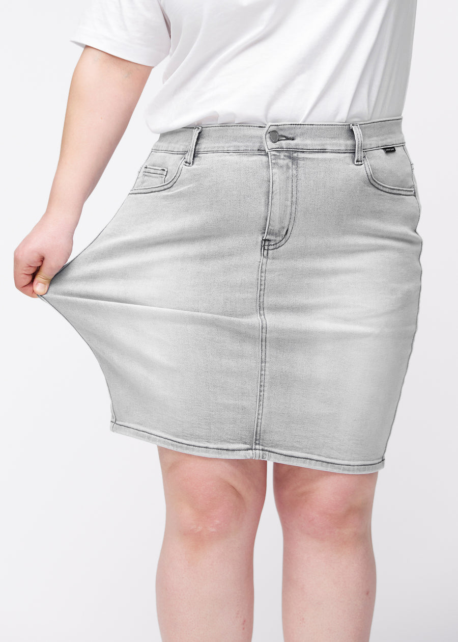 Plus-size model strækker lysegrå, tætsiddende og knælang denimnederdel ved låret for at vise stretch.