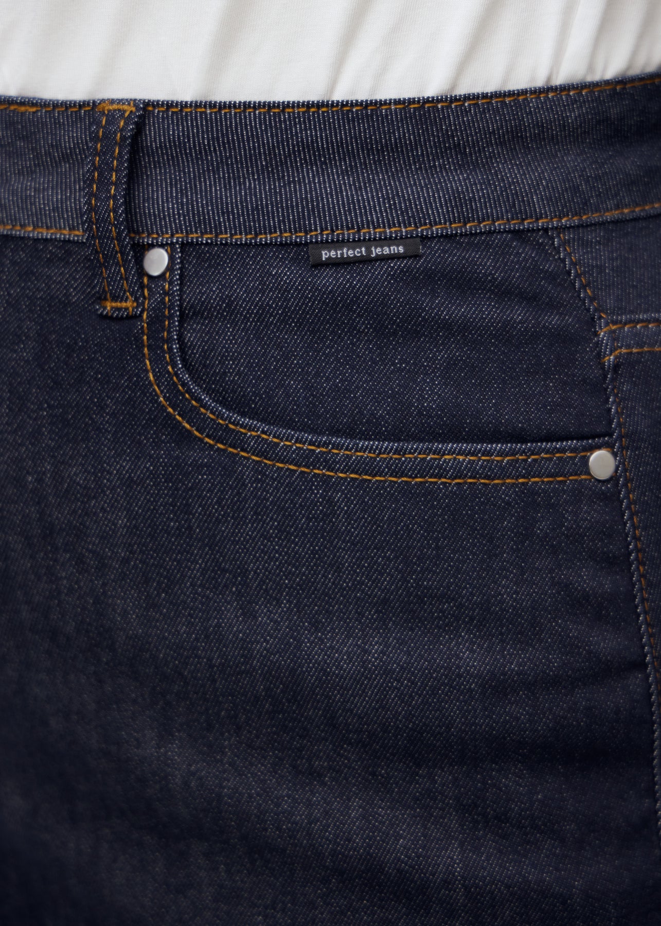 Nahaufnahme von dunkelblauem denim med perfect jeans logoetikett ved forlommekanten på plus-size-model.