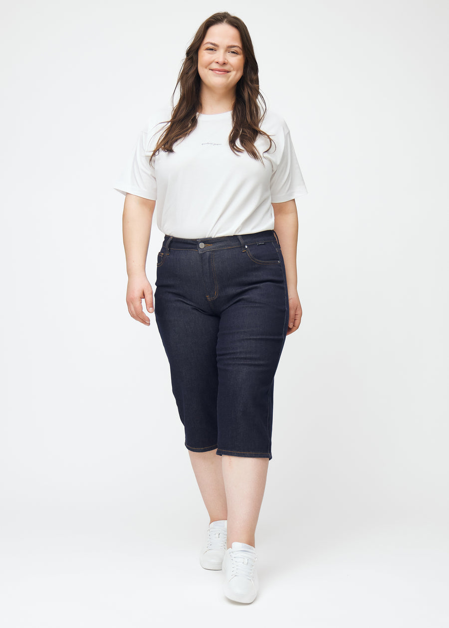 Ganzkörperbild eines Plus-Size-Models in tief dunkelblauen Denim-Capris für Damen in der Farbe Midnights mit Regular-Passform.