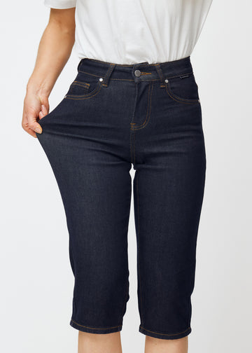 Model dehnt tief dunkelblaue Denim-Capris für Damen in der Farbe Midnights am Oberschenkel, um den Stretch des Materials zu zeigen.