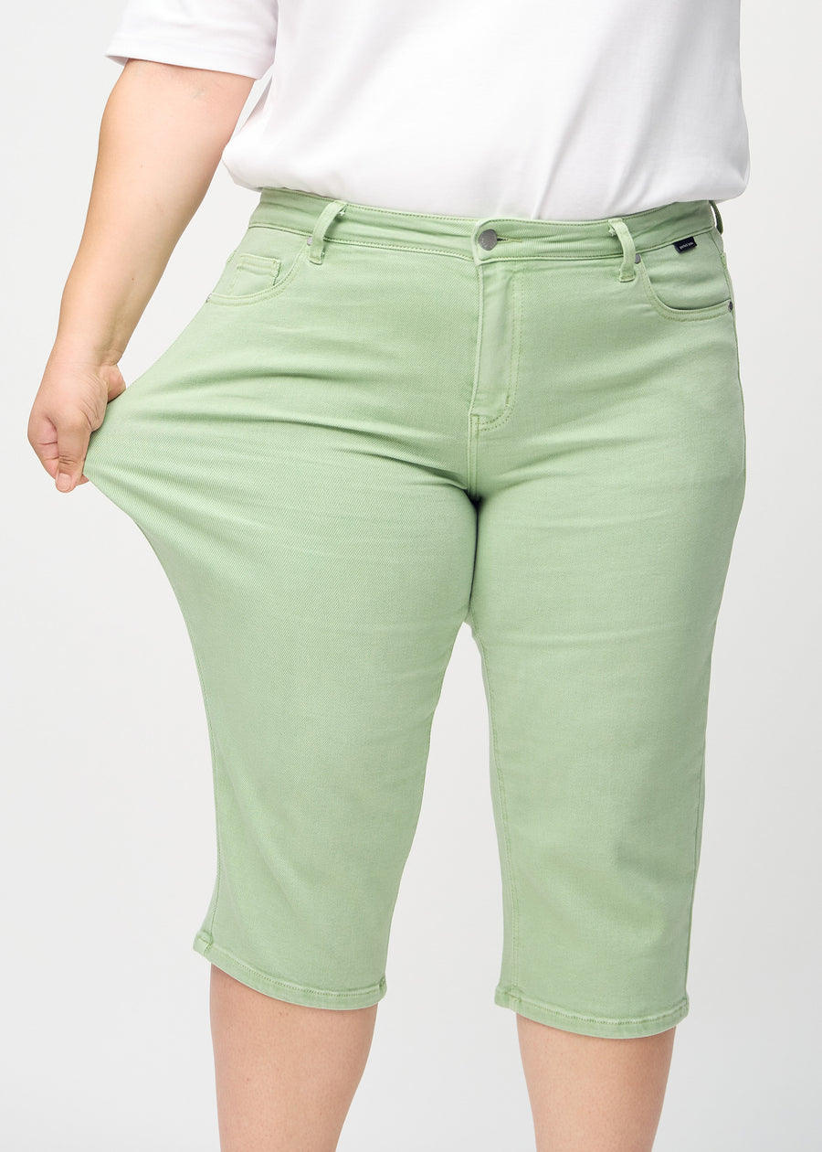 Ein Plus-Size-Model zieht die Capris am Oberschenkel, um den Stretch zu zeigen.