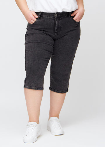 Dunkelgraue Denim-regular-Capris, Modellname Shadows, die eng am Bein anliegen und bei einem Plus-Size-Model knapp unter dem Knie enden, von vorn gesehen.