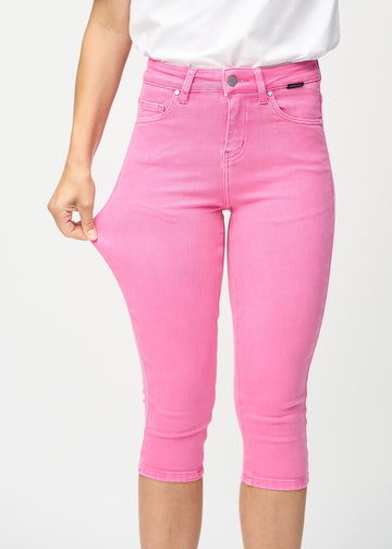 Skinny-Capris für Damen in pastellrosa Jeansstoff, Farbe Flamingos. Ein Model dehnt den Stoff, um den Stretch zu zeigen.