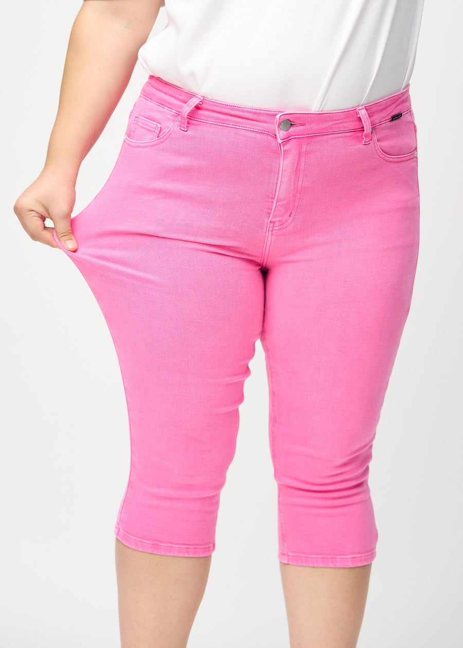 Skinny-Capris für Damen in pastellrosa Jeansstoff, Farbe Flamingos. Ein Plus-Size-Model dehnt den Stoff, um den Stretch zu zeigen.