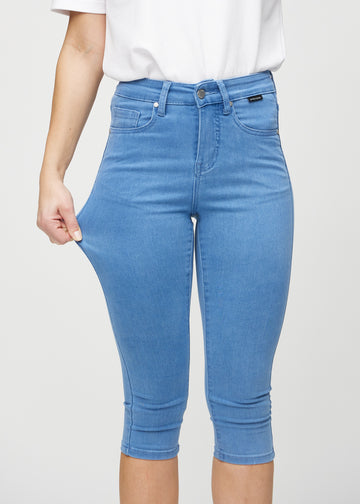 Skinny-Capris für Damen in blauem Jeansstoff, Farbe Geraniums. Ein Model dehnt den Stoff, um den Stretch zu zeigen.