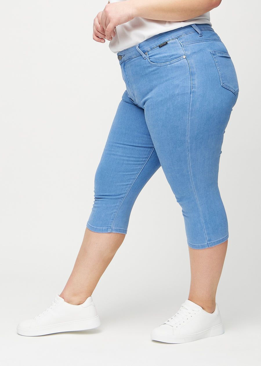 Skinny-Capris für Damen in blauem Jeansstoff, Farbe Geraniums. Seitenansicht an einem Plus-Size-Model, die figurbetonte Passform ist zu sehen.