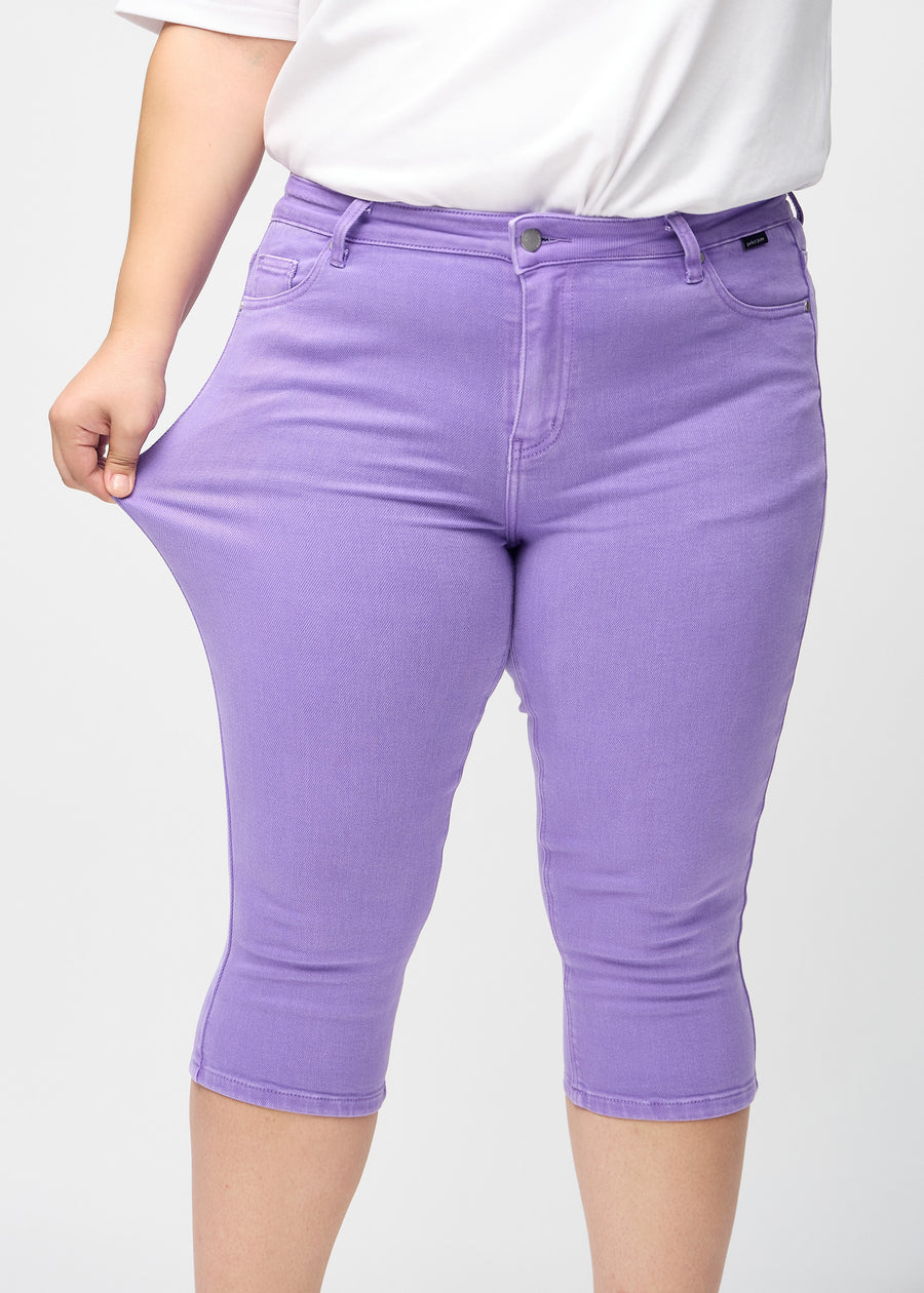 Skinny-Capris für Damen in pastellviolettem Jeansstoff, Farbe Lavenders. Ein Plus-Size-Model dehnt den Stoff, um den Stretch zu zeigen.