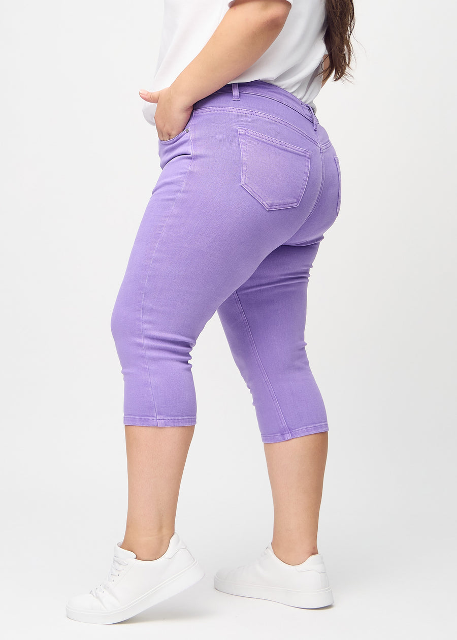 Skinny-Capris für Damen in pastellviolettem Jeansstoff, Farbe Lavenders. Seitenansicht an einem Plus-Size-Model, die figurbetonte Passform ist zu sehen.