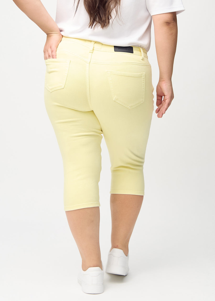Hellgelbe skinny Capris, von hinten gesehen, an einem Plus-Size-Model, sodass das gesamte Produkt zu sehen ist.