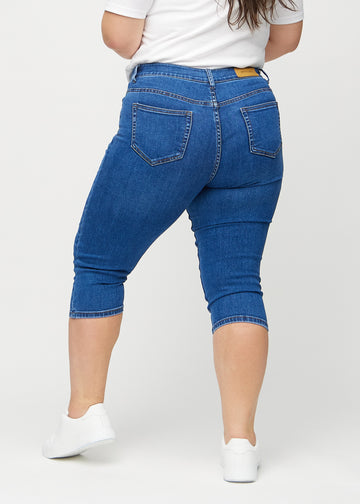 Skinny-Capris für Damen in dunkelblauem Denim, Farbe Oceans. Rückansicht an einem Plus-Size-Model, zeigt die Passform und Gesäßtaschen.
