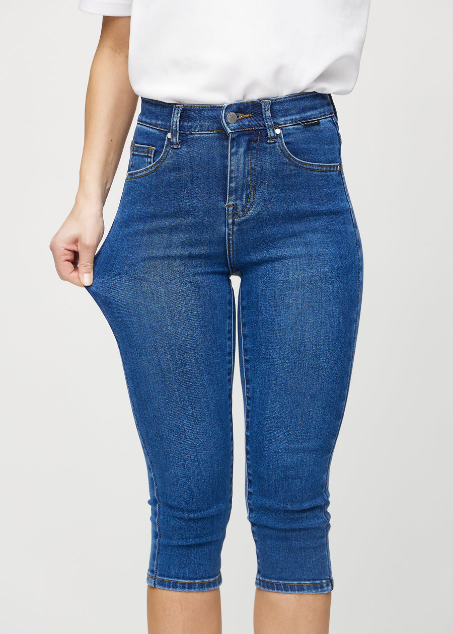 Skinny-Capris für Damen in dunkelblauem Denim, Farbe Oceans. Ein Model dehnt den Stoff, um den Stretch zu zeigen.
