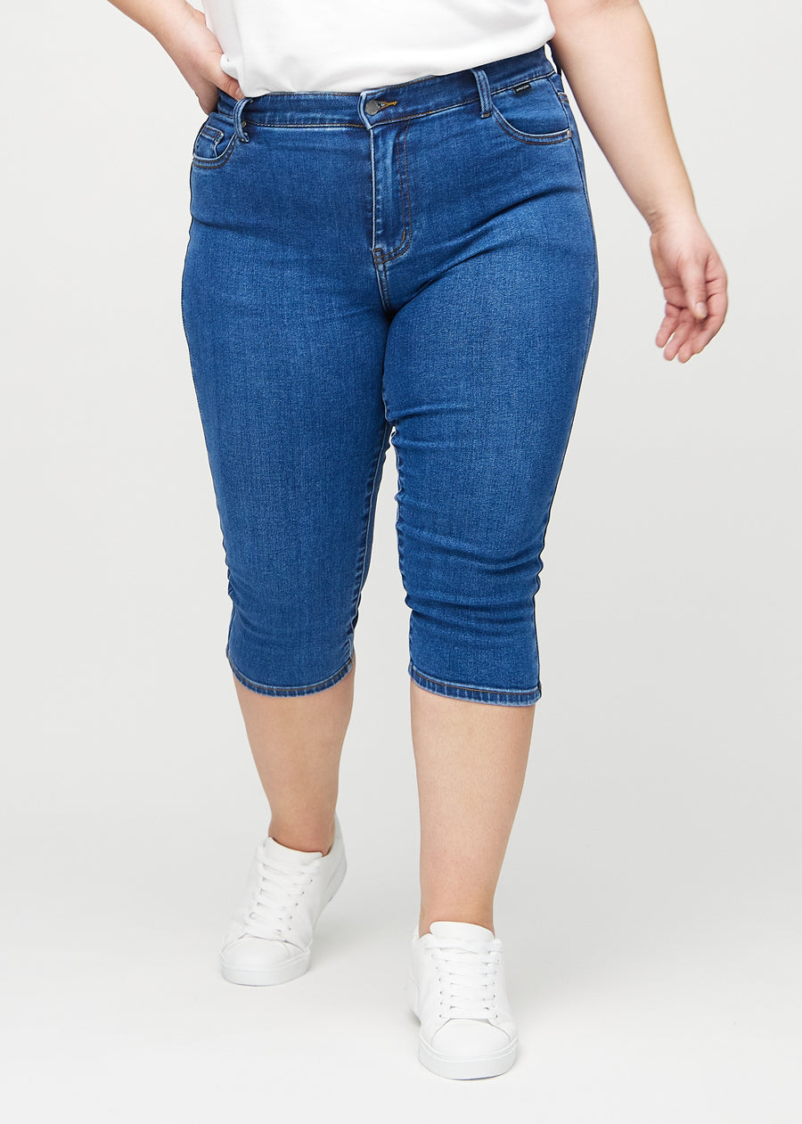 Skinny-Capris für Damen in dunkelblauem Denim, Farbe Oceans. Vorderansicht an einem Plus-Size-Model, eng geschnitten bis knapp unter das Knie.