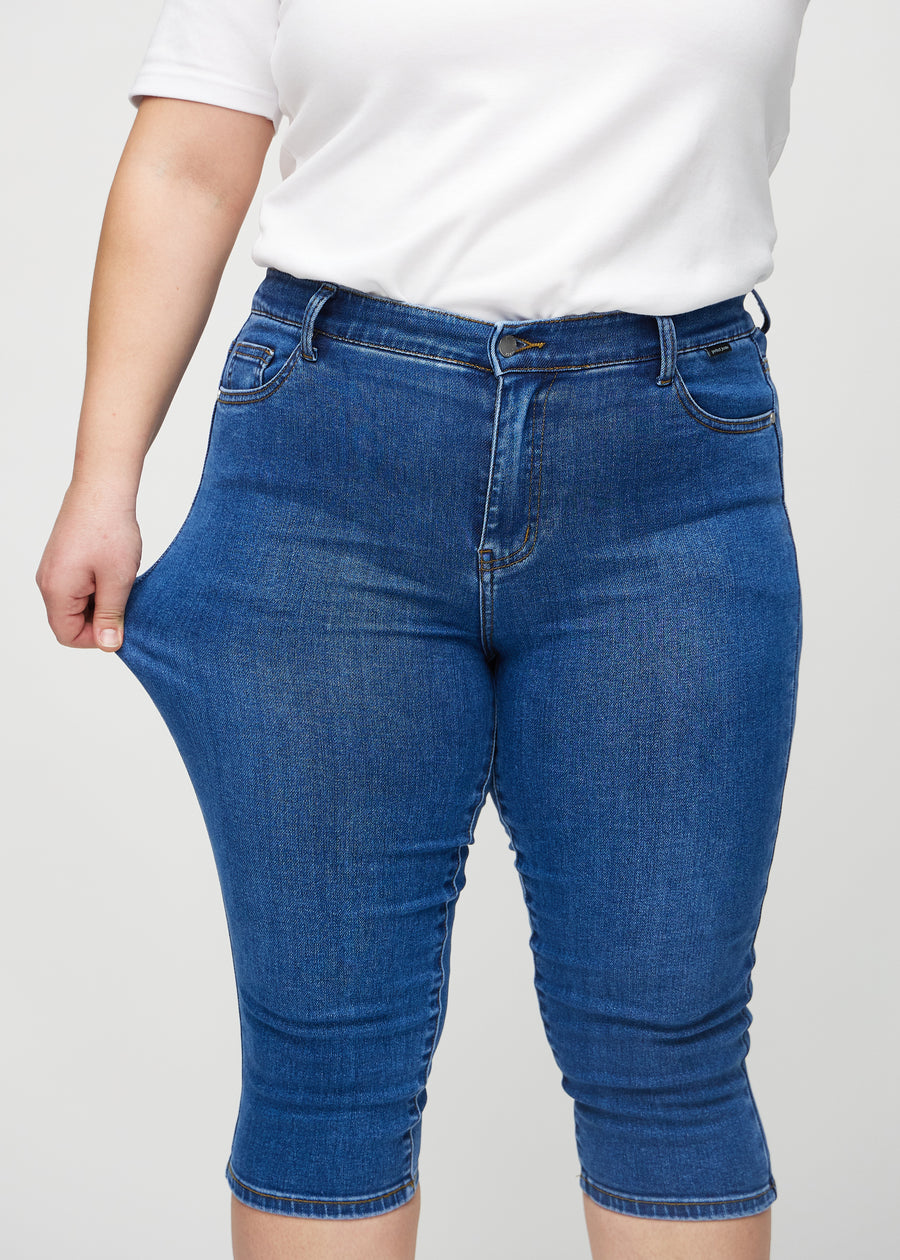 Skinny-Capris für Damen in dunkelblauem Denim, Farbe Oceans. Ein Plus-Size-Model dehnt den Stoff, um den Stretch zu zeigen.