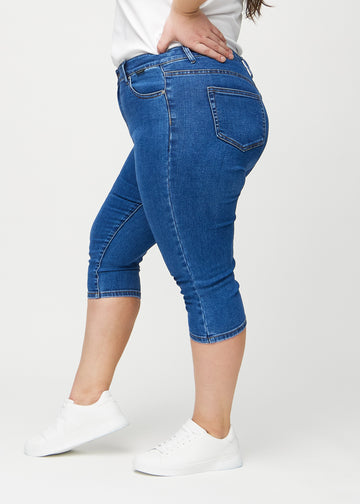 Skinny-Capris für Damen in dunkelblauem Denim, Farbe Oceans. Seitenansicht an einem Plus-Size-Model, die figurbetonte Passform ist zu sehen.