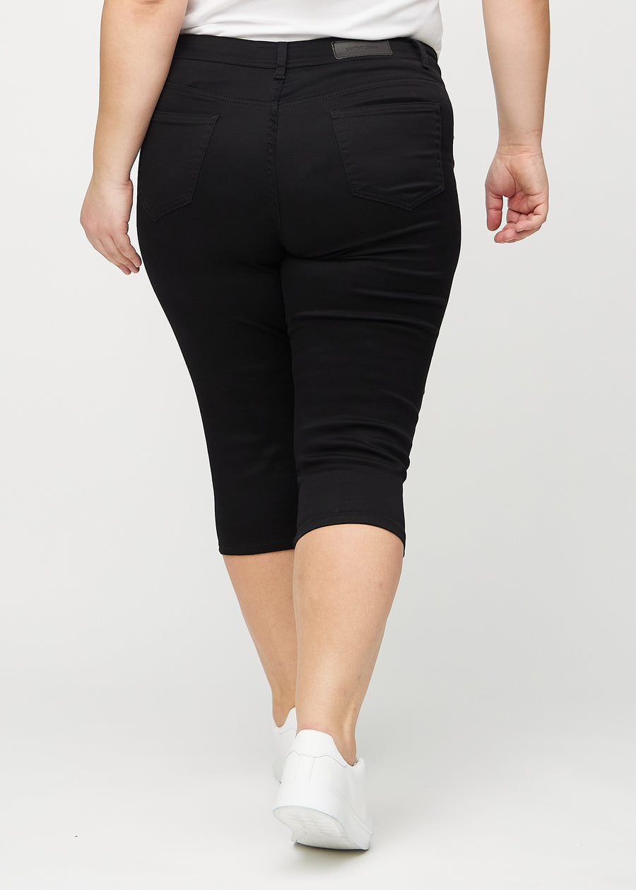 Schwarze skinny Capris von hinten an einem Plus-Size-Model gesehen, sodass man das gesamte Produkt sehen kann.