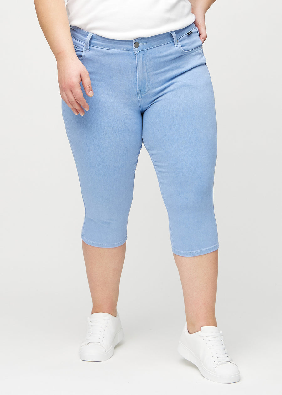 Skinny-Capris für Damen in hellblauem Jeansstoff, Farbe Skies. Vorderansicht an einem Plus-Size-Model, eng geschnitten bis knapp unter das Knie.