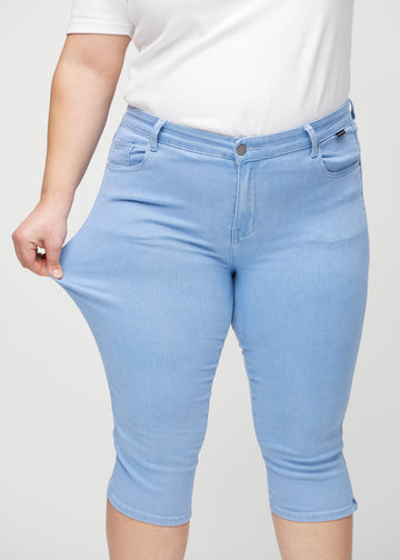 Skinny-Capris für Damen in hellblauem Jeansstoff, Farbe Skies. Ein Plus-Size-Model dehnt den Stoff, um den Stretch zu zeigen.