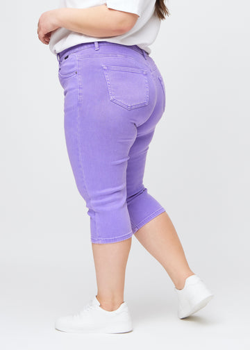 Slim-Capris für Damen aus pastellviolettem Jeansstoff, Farbe Lavenders. Seitenansicht an einem Plus-Size-Model, figurbetonter Schnitt und mittelhoher Bund (Mid Rise).