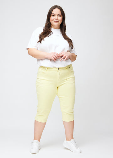 Ganzkörperbild eines Plus-Size-Models in hellgelben slim Capris.
