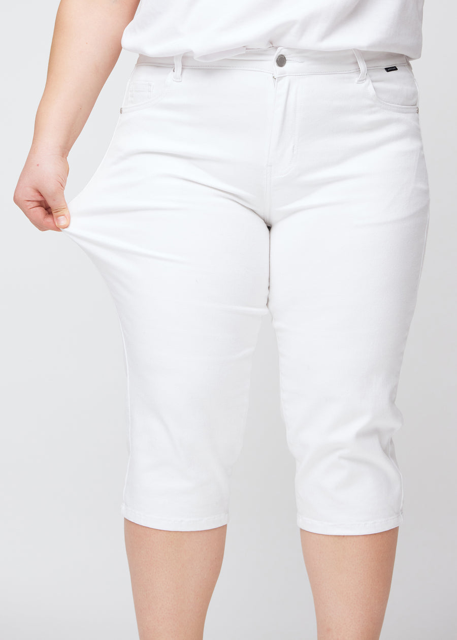 Slim-Capris für Damen aus weißem Jeansstoff, Farbe Marguerites. Ein Plus-Size-Model dehnt den Stoff am Oberschenkel, um die Flexibilität zu zeigen.