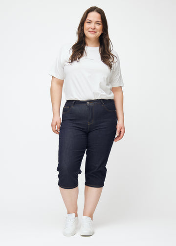 Ganzkörperbild eines Plus-Size-Models in tief dunkelblauen Denim-Capris für Damen in der Farbe Midnights mit Slim-Passform.