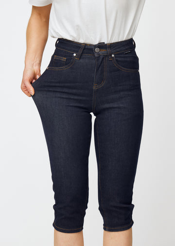 Model dehnt tief dunkelblaue Denim-Capris für Damen in der Farbe Midnights am Oberschenkel, um den Stretch des Materials zu zeigen.