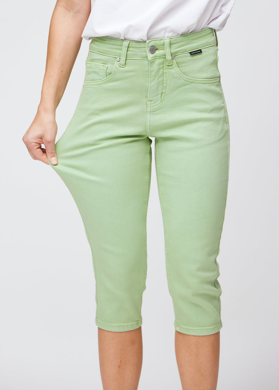 Slim-Capris für Damen aus pastellhellgrünem Jeansstoff, Farbe Mints. Ein Model dehnt den Stoff am Oberschenkel, um die Flexibilität zu zeigen.