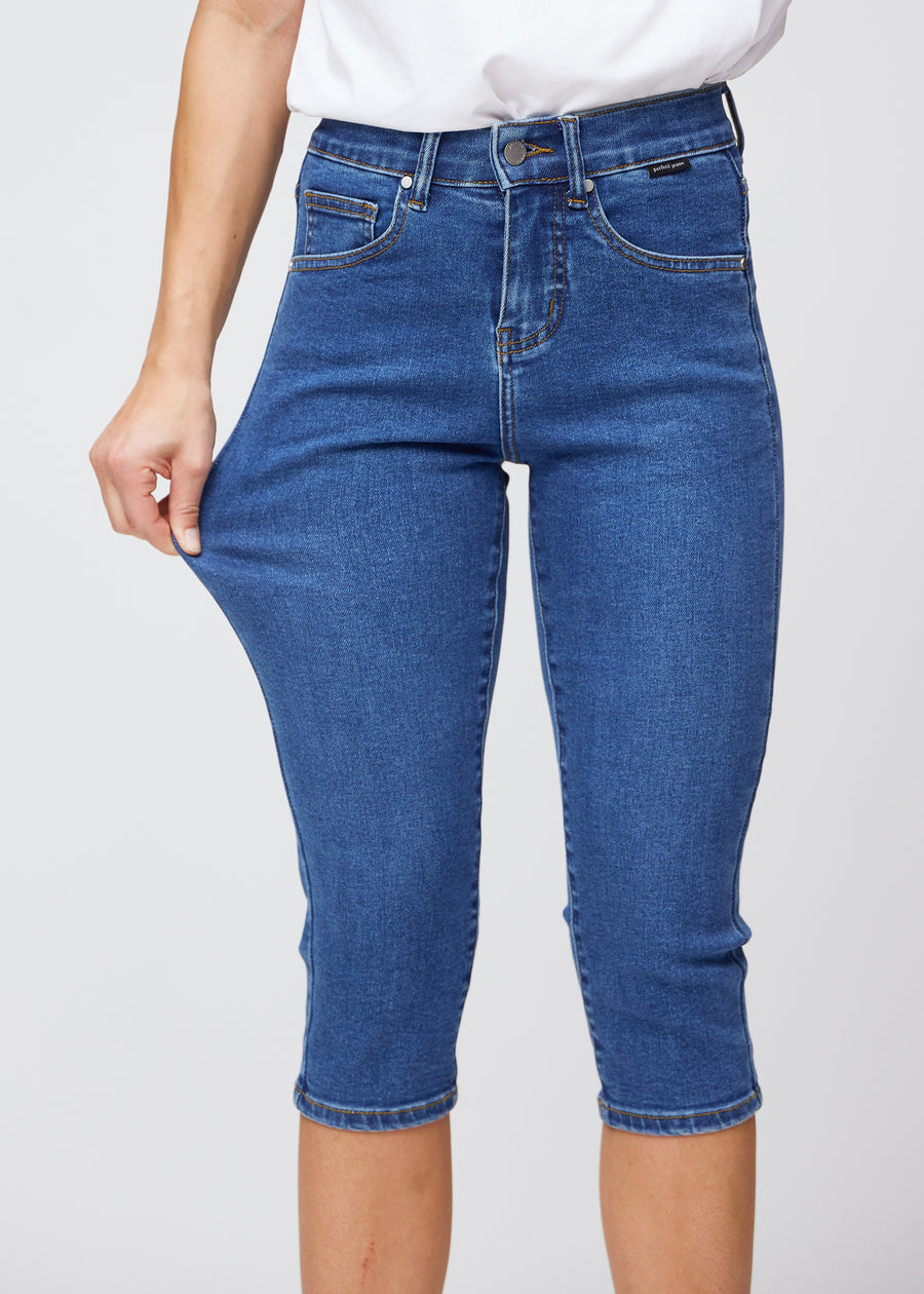 Slim-Capris für Damen aus dunkelblauem Denim, Farbe Oceans. Ein Model dehnt den Stoff am Oberschenkel, um die Flexibilität zu zeigen.