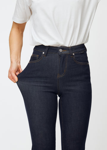 Das Model dehnt die tief dunkelblaue Denim jeans für Damen in der Farbe Midnights am Oberschenkel, um die Dehnbarkeit des Materials zu zeigen.