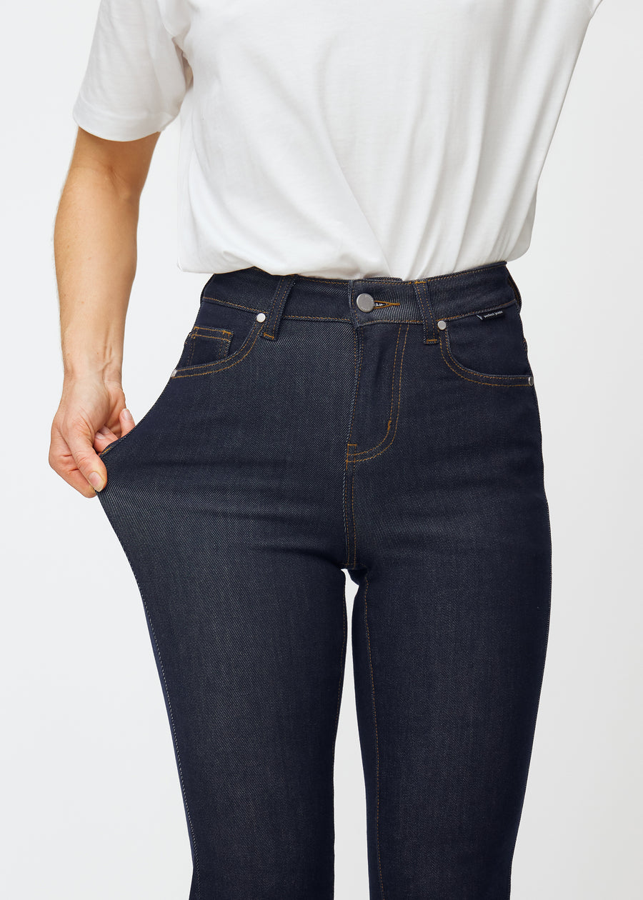 Das Model dehnt die tief dunkelblaue Denim jeans für Damen in der Farbe Midnights am Oberschenkel, um die Dehnbarkeit des Materials zu zeigen.