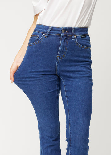 Dunkelblaue Mid-Rise-Bootcut-Jeans in der Farbe Oceans. Ein Model zieht am Jeansstoff am Oberschenkel, um den Stretch zu zeigen.